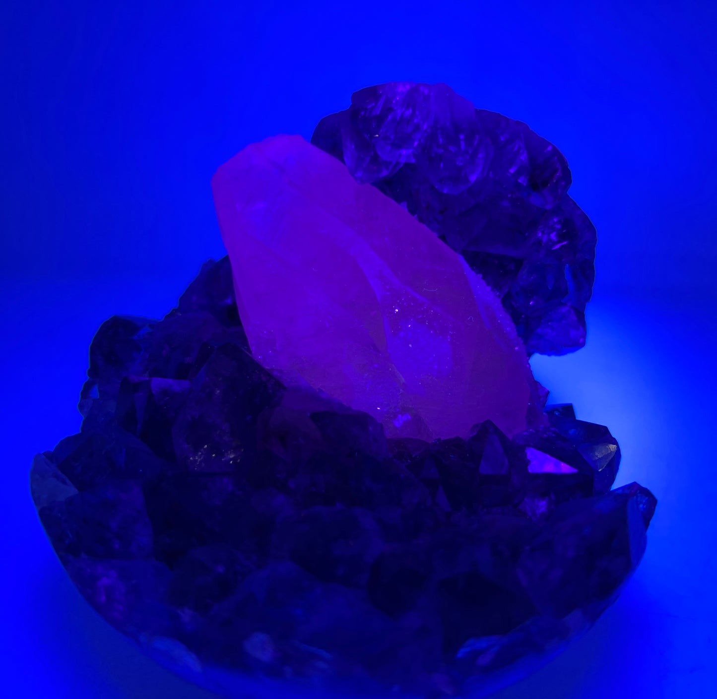 A natural amethyst geode sphere with a large sparkly coated calcite in the centre, from Brazil, under ultraviolet light.
