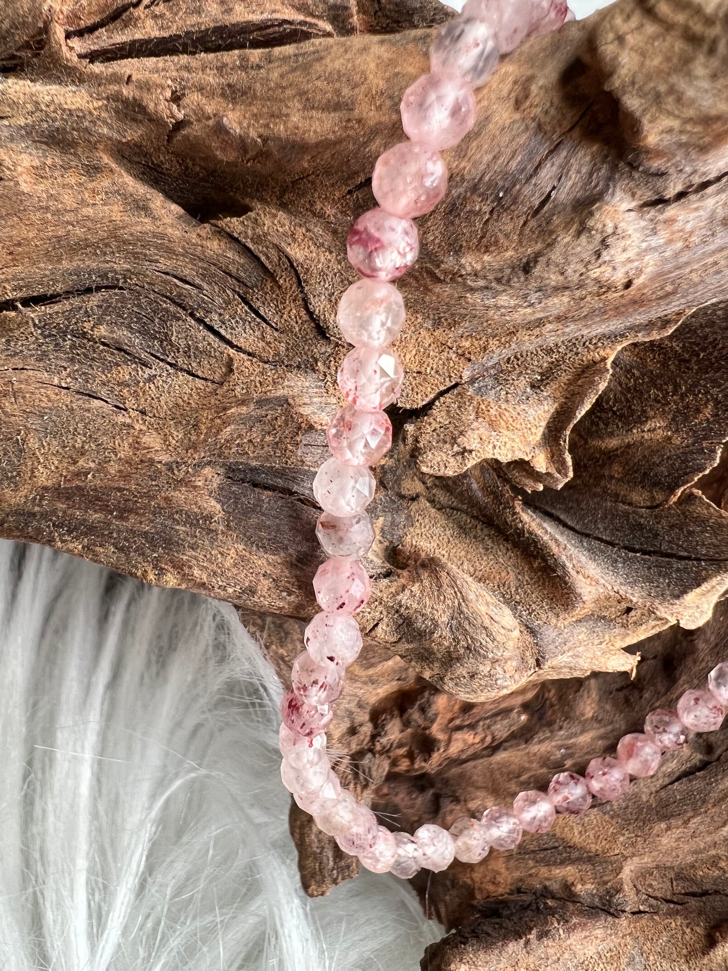 A delicate pink Strawberry Quartz bracelet with faceted beads, displayed on a rustic wooden background.