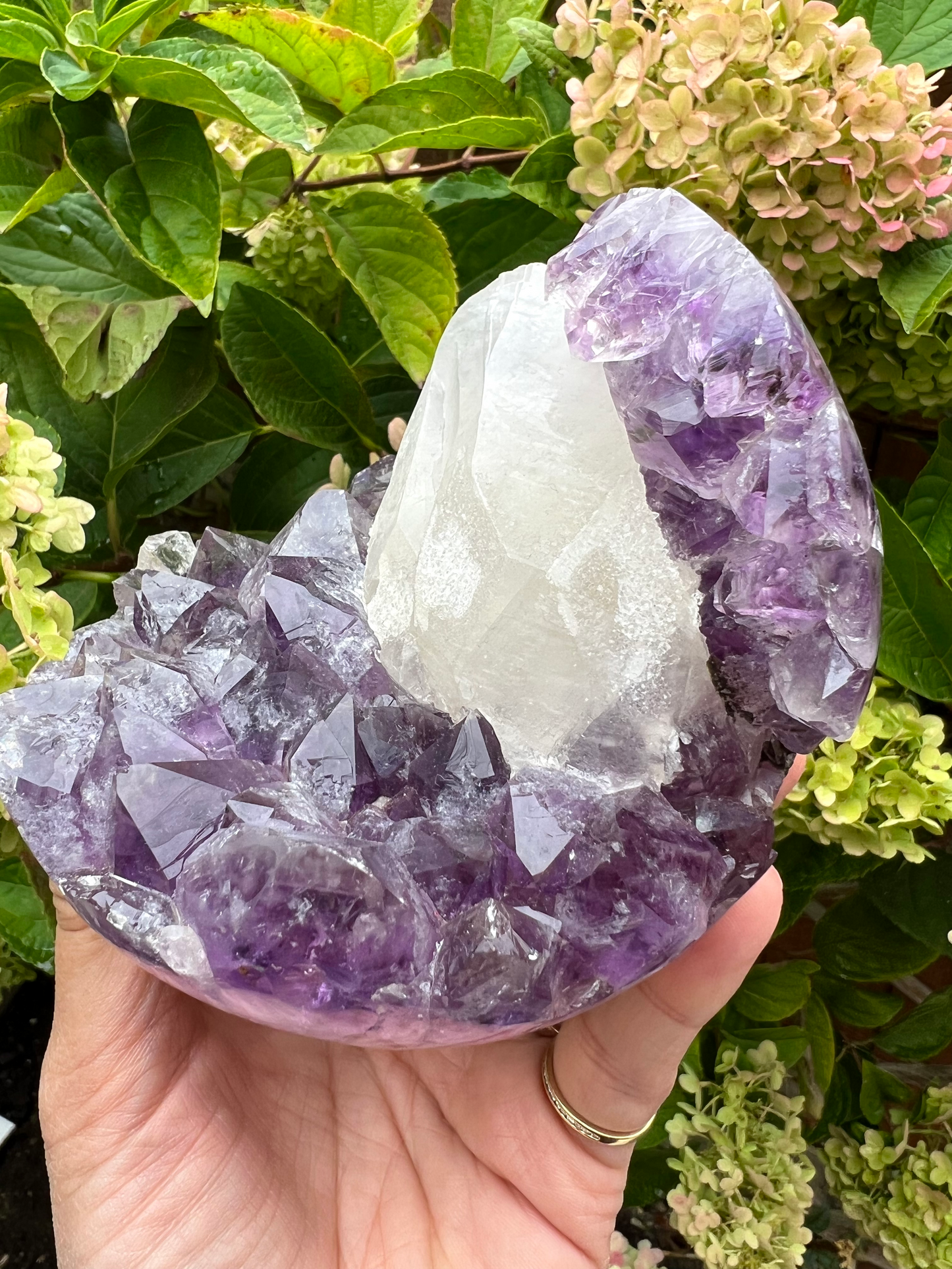 A natural amethyst geode sphere with a large sparkly coated calcite in the centre, from Brazil.