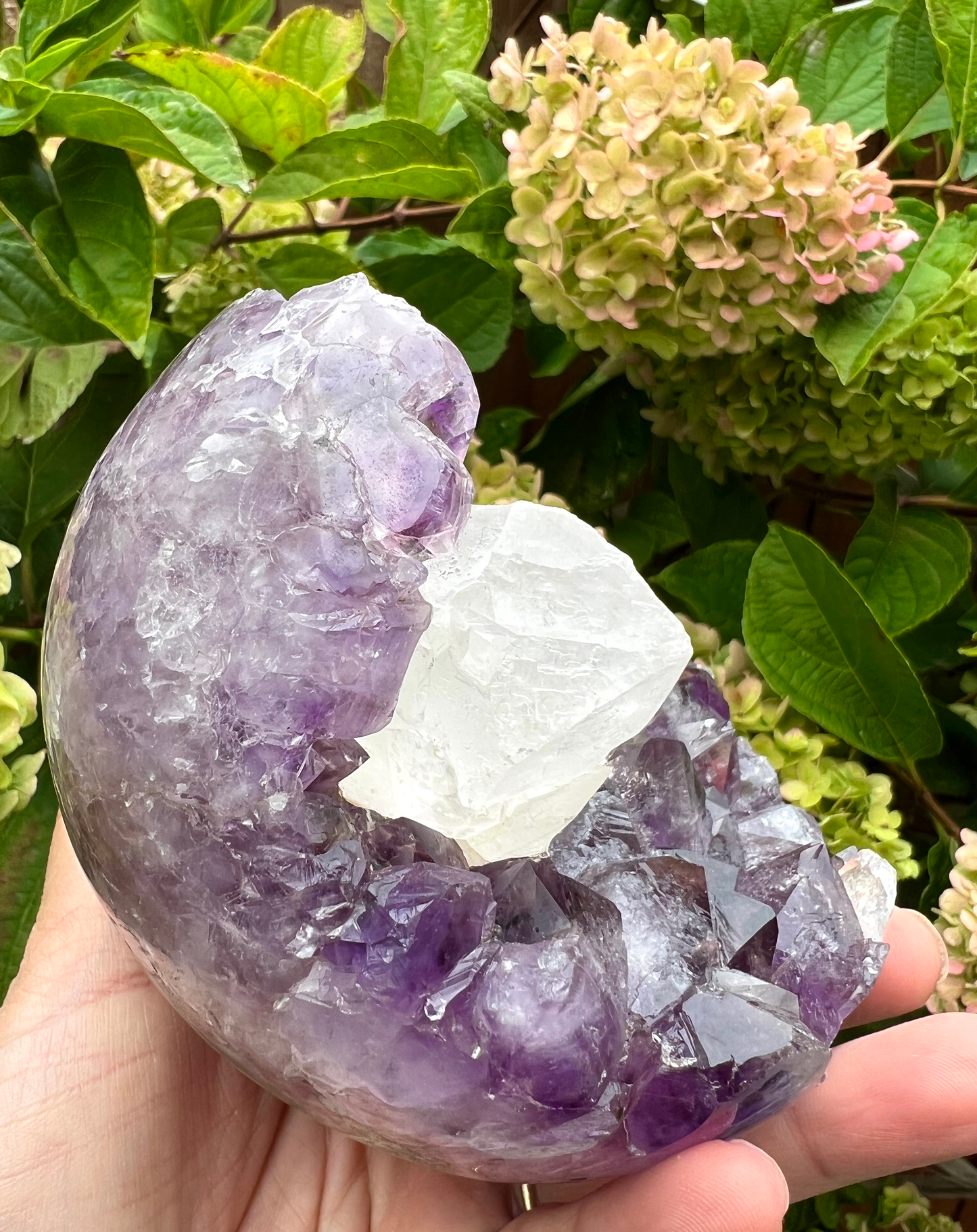 A natural amethyst geode sphere with a large sparkly coated calcite in the centre, from Brazil.