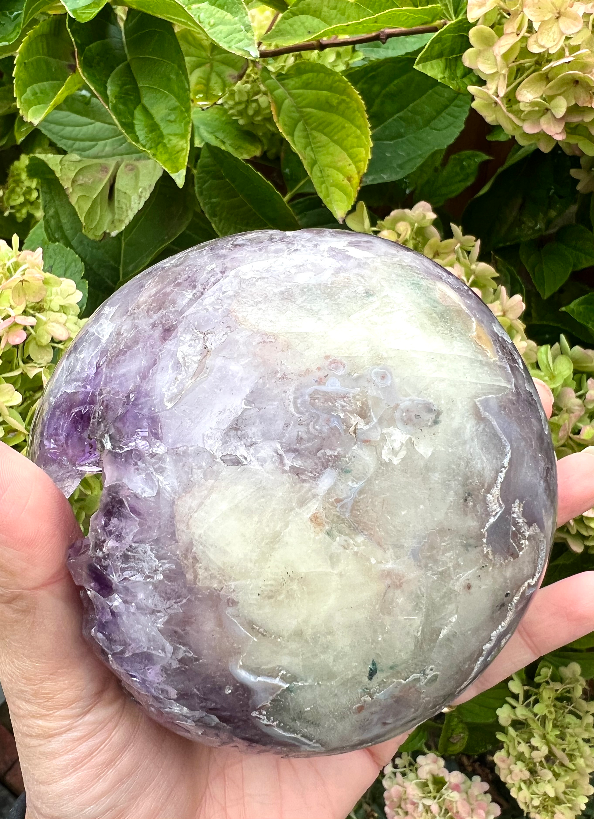 A natural amethyst geode sphere with a large sparkly coated calcite in the centre, from Brazil.